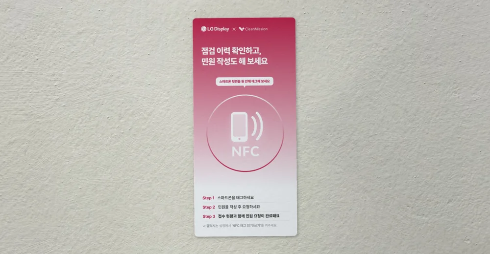 흰 벽에 붙은 LG디스플레이 NFC 태그 카드. 카드 가운데에 휴대폰을 대는 NFC 동그라미가 있다