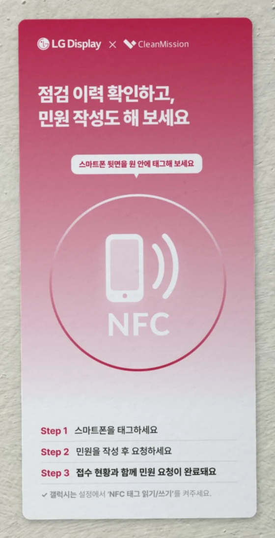 흰 벽에 붙은 LG디스플레이 NFC 태그 카드. 점검 이력 확인하고, 민원 작성도 해 보세요 라고 적혀 있다